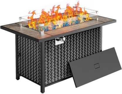 Outdoor rectangular fire pit table with a black woven wicker-style cabinet body, glass wind guard, orange and yellow flames, blue decorative stones, and a separate dark gray back panel leaning against the base on a white background.