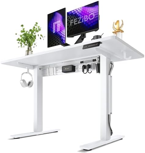 A white electric height-adjustable standing desk with two computer monitors, a small potted plant, a pair of headphones hanging from the side, and a gold trophy on top, shown on a clean white background.