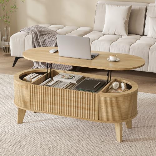 An oval-shaped wooden coffee table with a woven rattan lower storage cabinet, styled in a bright living room with a laptop and cup on top.