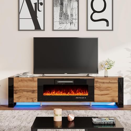 A modern electric fireplace TV stand in a living room setting, featuring a wood grain finish, black side panels, and a glowing orange fire effect inside. A black flat-screen TV sits on top, with framed wall art and a coffee table below.