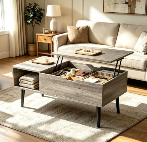 A modern lift-top coffee table in a warm gray wood finish, shown in a bright, modern living room. The table is open, revealing a storage compartment with folded blankets and a tray organizer on the lift-up top.