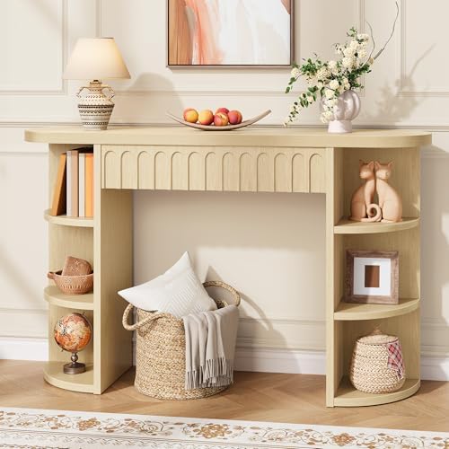 A light beige console table with built-in open shelving, styled in a warm, neutral-toned room. The table is decorated with a patterned lamp, a bowl of fruit, a vase of white flowers, books, baskets, and decorative figurines.