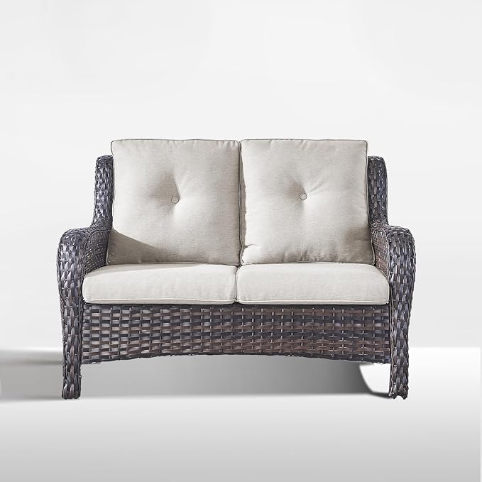 A two-seater wicker loveseat with dark gray woven frames and light beige tufted cushions, shown against a plain light gray background.