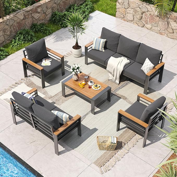 Outdoor patio furniture set with gray cushions and wooden accents on a stone patio.