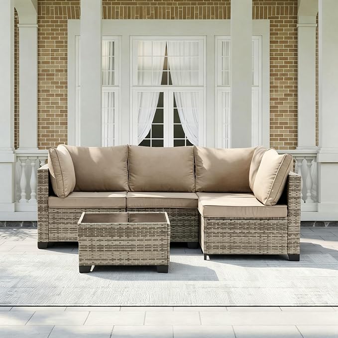 A 5-piece outdoor sectional sofa set with a matching rectangular coffee table, featuring beige cushions and woven wicker frames, set on a porch in front of a brick and white column building.