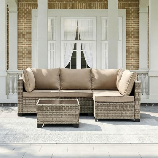 A 5-piece outdoor sectional sofa set with a matching rectangular coffee table, featuring beige cushions and woven wicker frames, set on a porch in front of a brick and white column building.