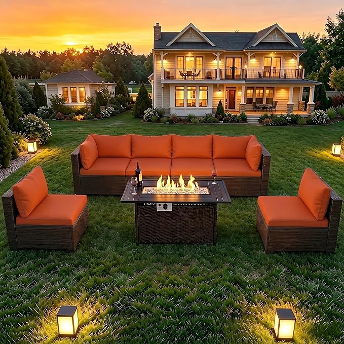 Outdoor patio furniture set on a grassy lawn in front of a two-story house at sunset, featuring a dark brown wicker-style sectional sofa, two matching armchairs, and a square fire pit table with visible flames.