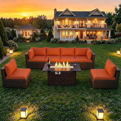 Outdoor patio furniture set on a grassy lawn in front of a two-story house at sunset, featuring a dark brown wicker-style sectional sofa, two matching armchairs, and a square fire pit table with visible flames.