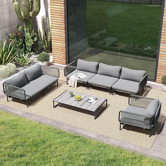 Outdoor patio set with gray cushions on a patio area with plants and a glass door.